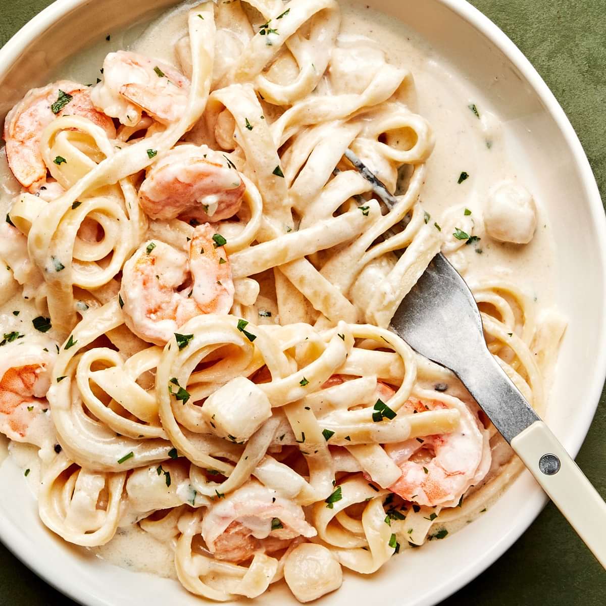 a bowl of homemade seafood fettuccine alfredo made with shrimp and scallops, sprinkled with parsley