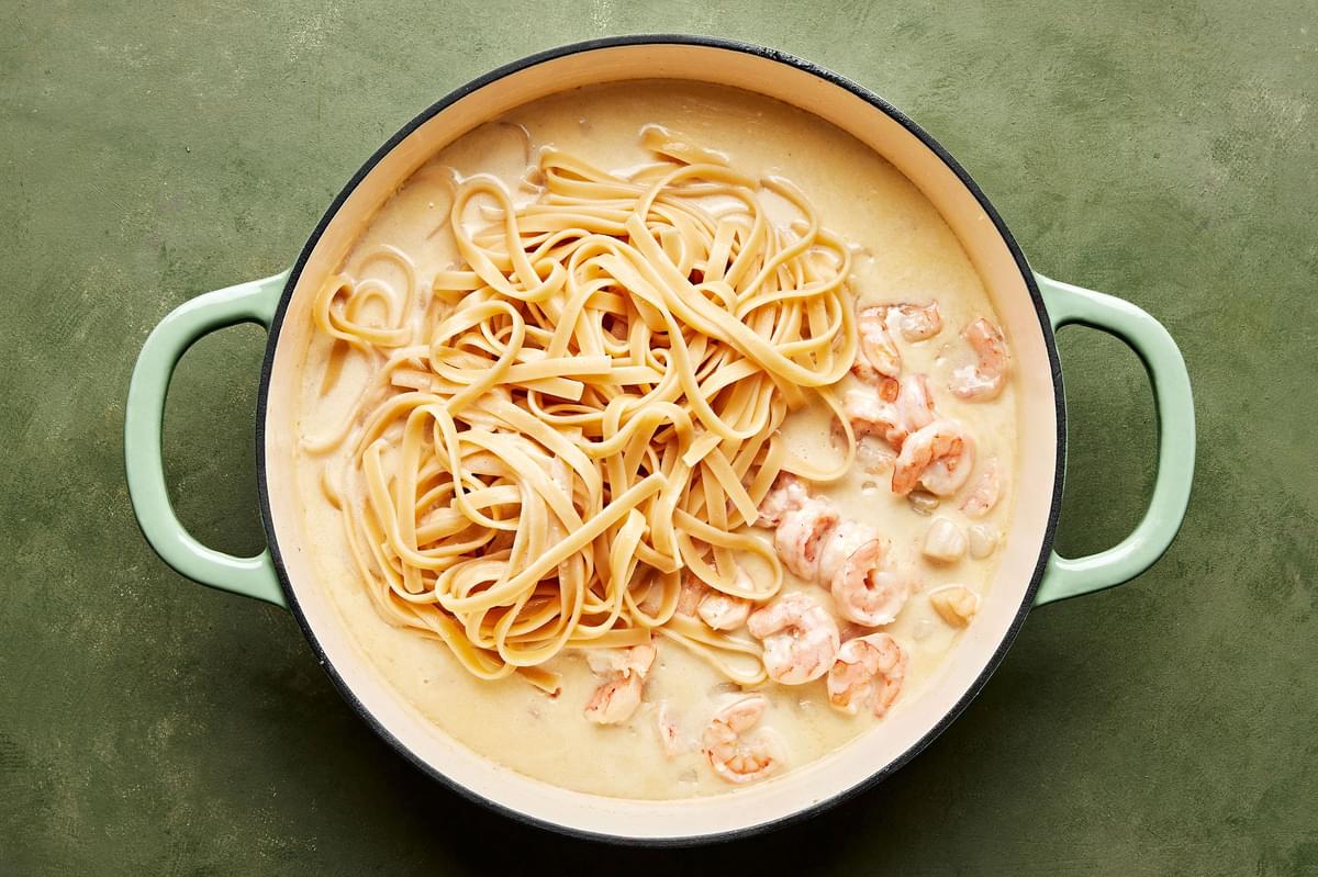 fettuccine noodles added to a skillet with seafood alfredo sauce