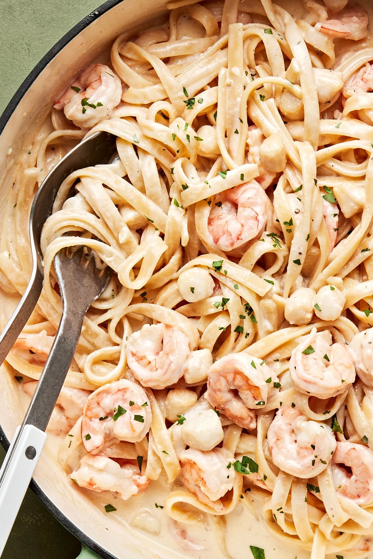 a skillet of homemade seafood fettuccine alfredo sprinkled with parsley made with scallops and shrimp