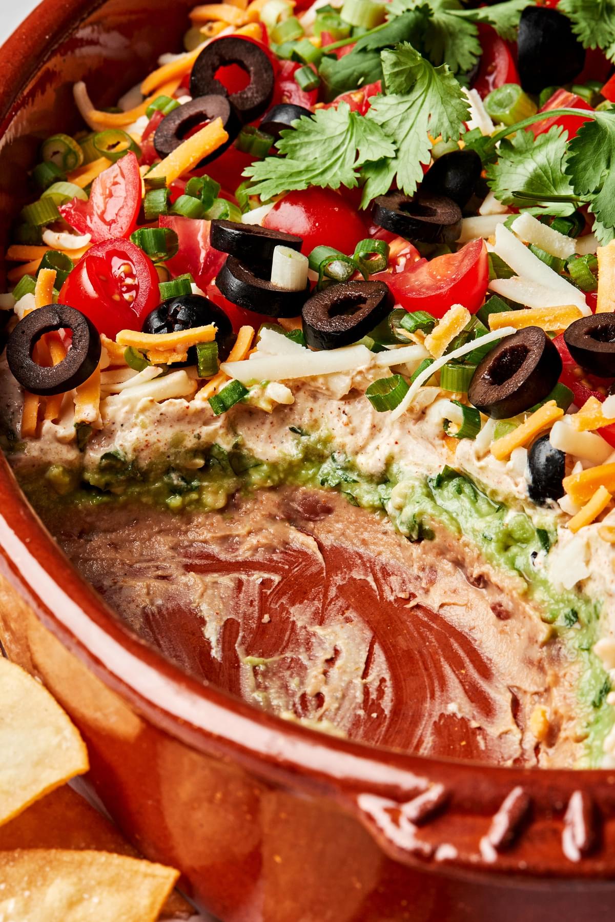 seven layer dip made with beans, sour cream, guacamole, cheese, olives, tomato, cilantro and green onions