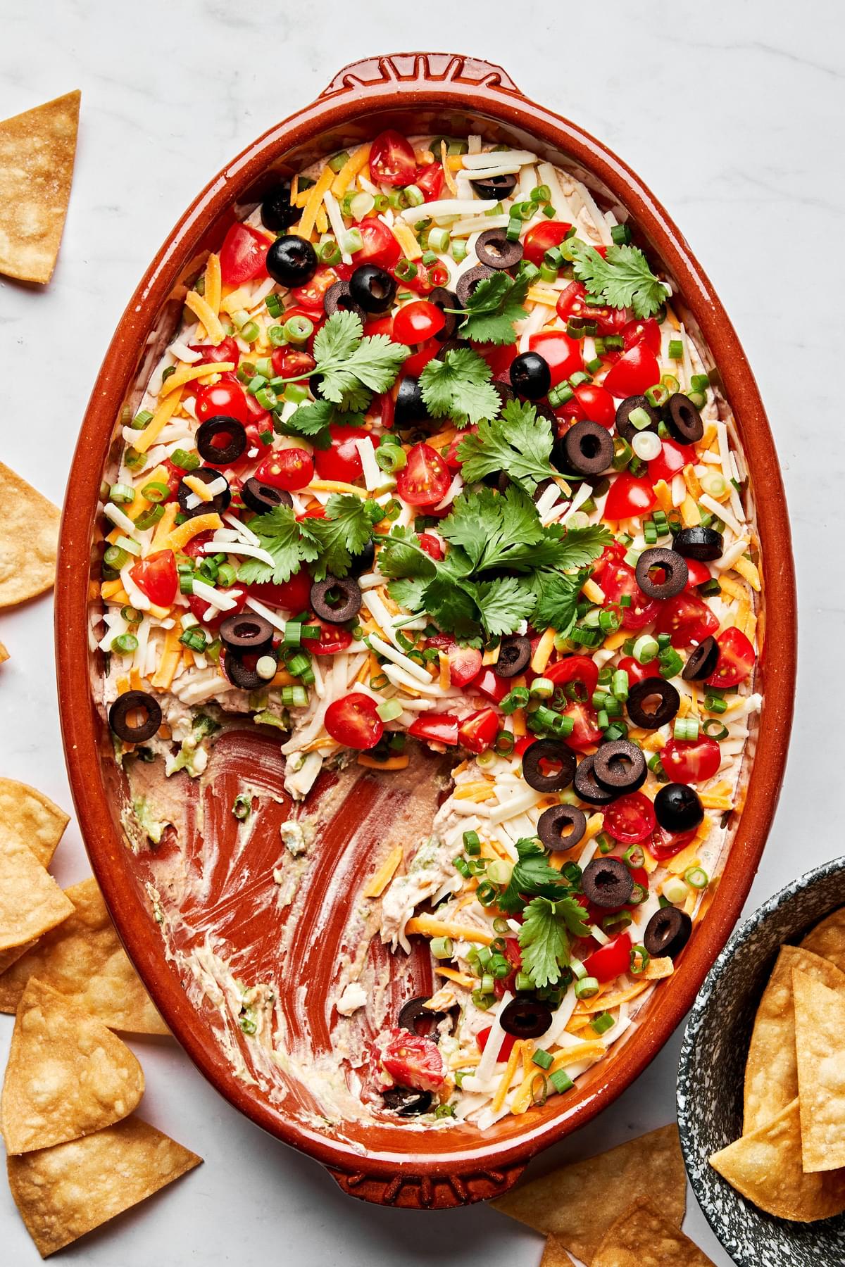 seven layer dip in a serving bowl surrounded by tortilla chips