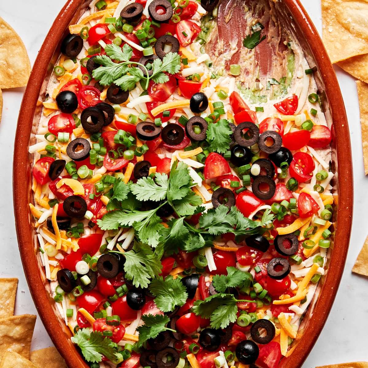 seven layer dip made with guacamole, refried beans, shredded cheese, sour cream, tomatoes, olives, green onion and cilantro
