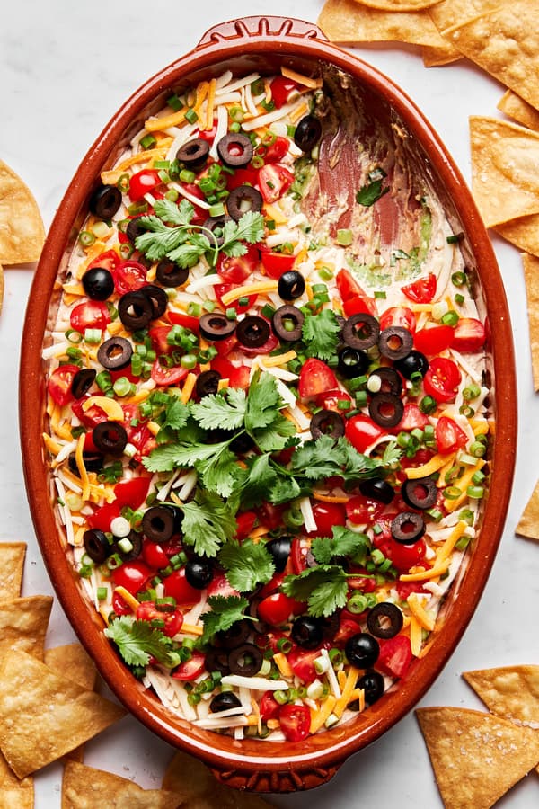 seven layer dip made with guacamole, refried beans, shredded cheese, sour cream, tomatoes, olives, green onion and cilantro