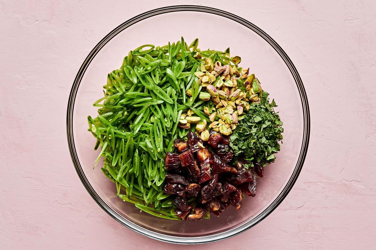 sliced snap peas, chopped dates, pistachios and mint leaves being tossed in a bowl