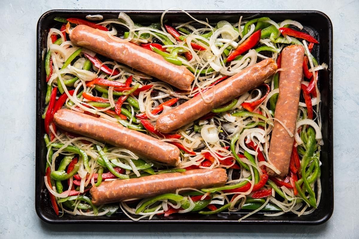 raw Italian sausage on a rimmed baking sheet with sliced onions and bell peppers