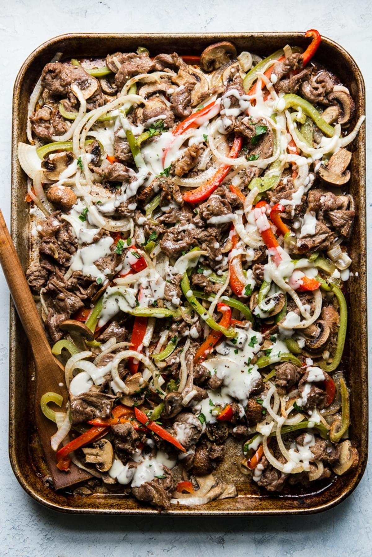 thinly sliced steak bell peppers and onions cooked on a sheet pan for Philly Cheese steak with provolone cheese sauce