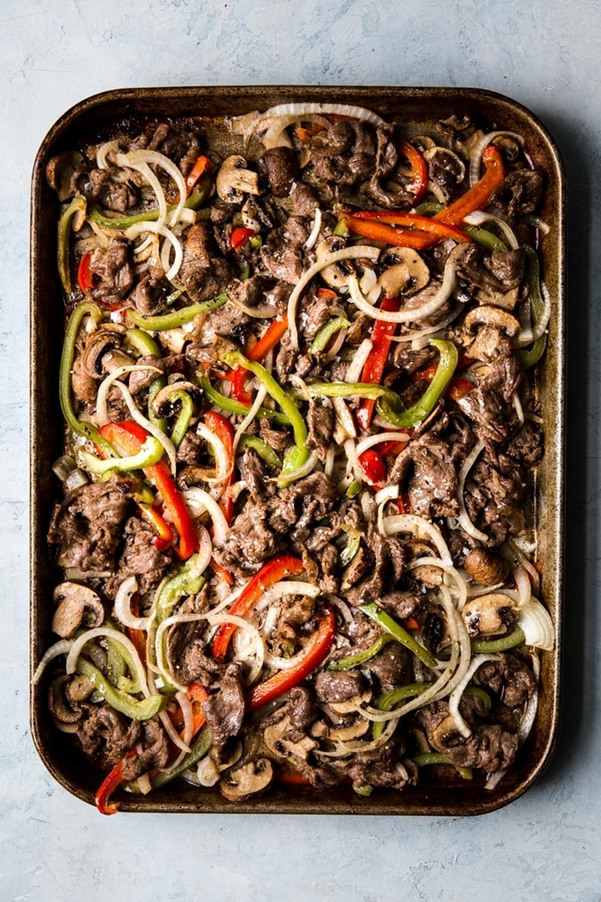 thinly sliced steak bell peppers and onions cooked on a sheet pan for Philly Cheese steak