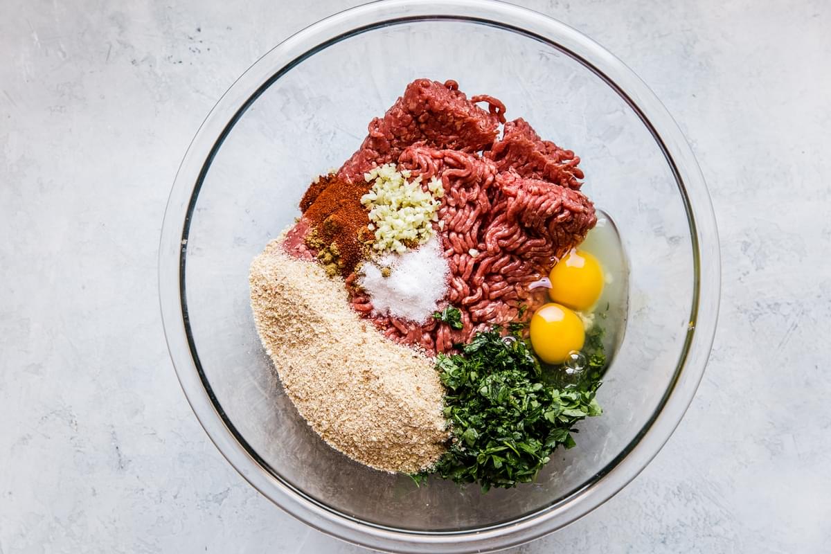 ingredients for harissa meatballs in a bowl, ground beef, eggs, bread crumbs and parsley