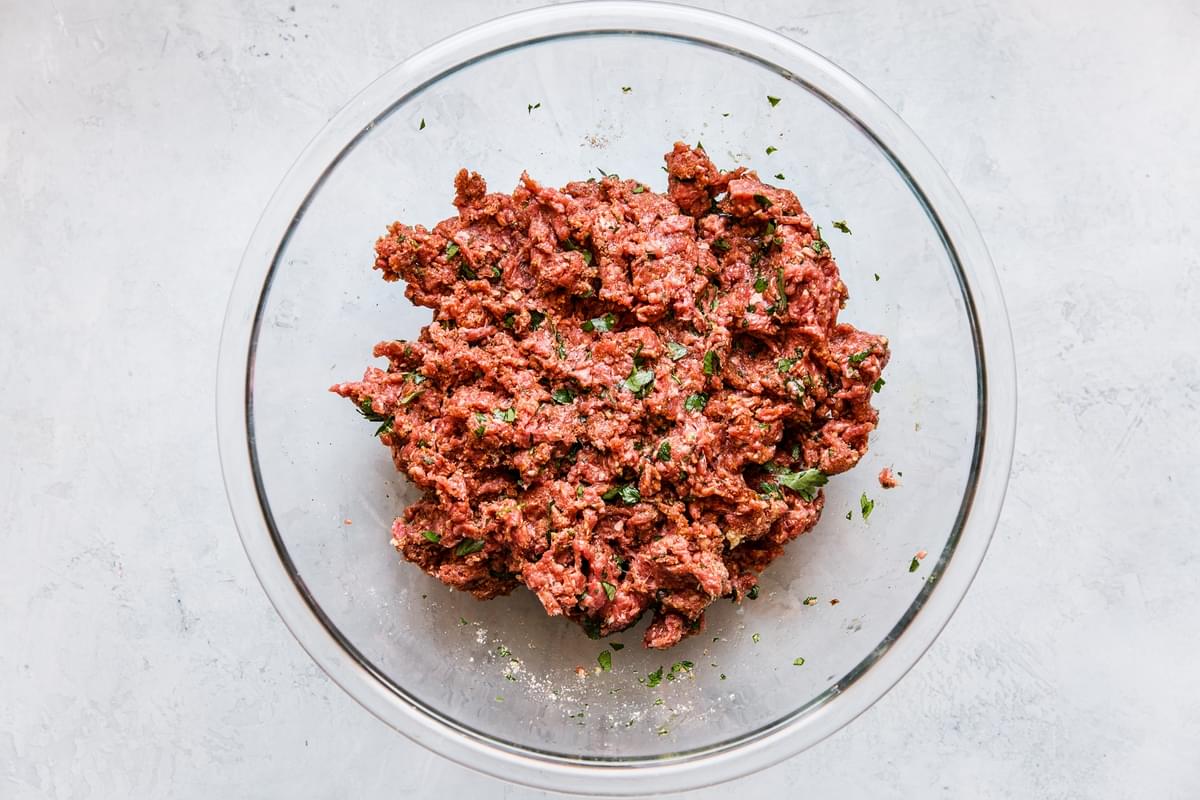 ingredients for harissa meatballs mixed up in a bowl, ground beef, eggs, bread crumbs and parsley