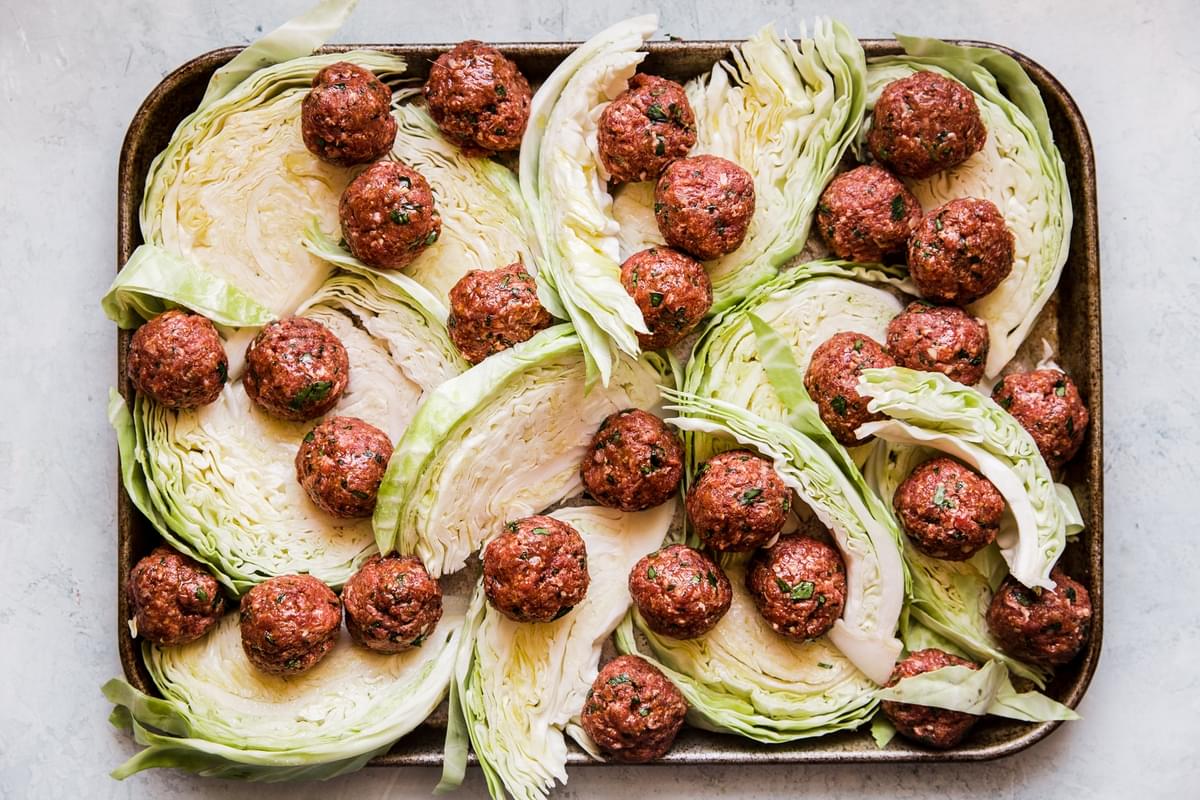 raw meatballs on a baking sheet with cabbage wedges