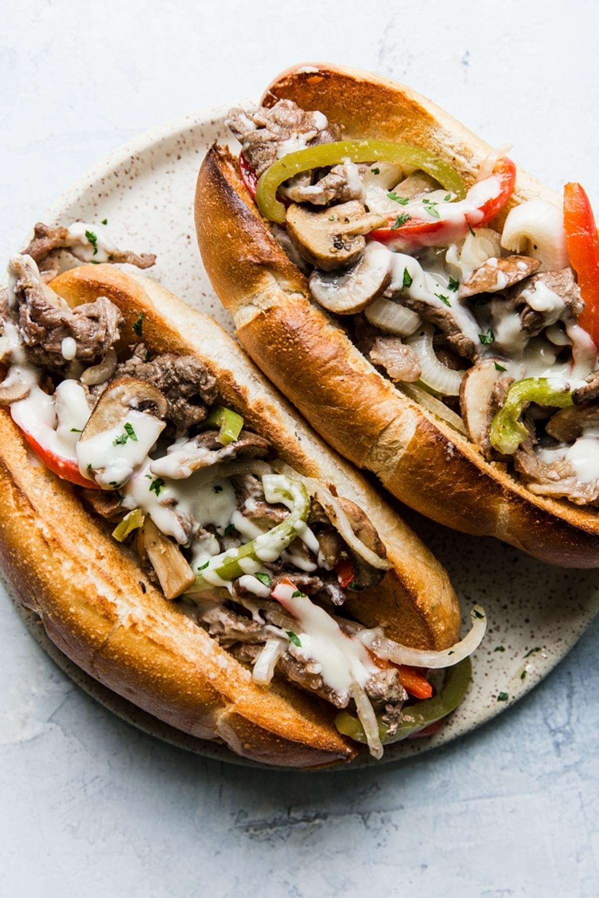 sheet pan philly cheesesteaks on hoagies made with sirloin steak, bell peppers, onions and mushrooms and cheese sauce