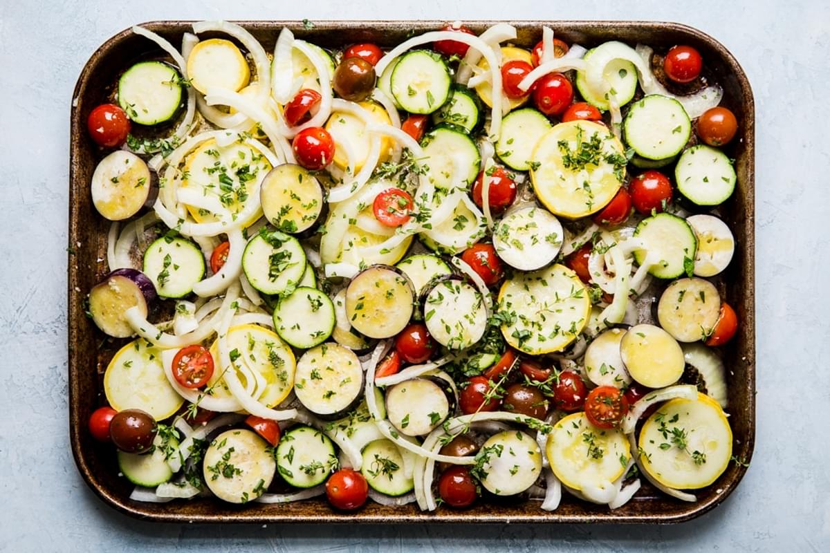 sliced yellow squash, zucchini, onions and tomatoes on a sheet pan for ratatouille