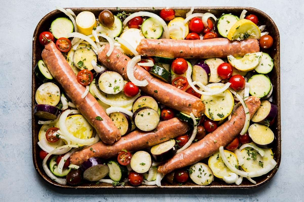 sliced yellow squash, zucchini, onions and tomatoes on a sheet pan for ratatouille with sausage