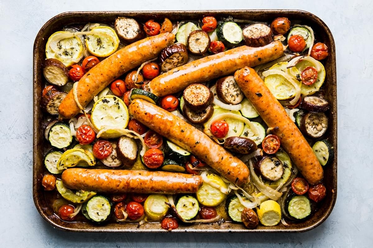 cooked sliced yellow squash, zucchini, onions and tomatoes on a sheet pan for ratatouille with sausage
