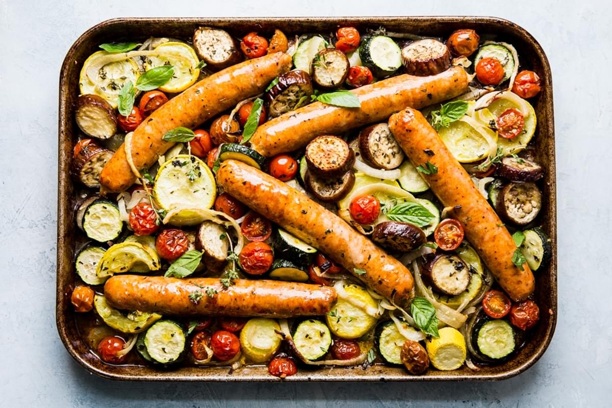 cooked sliced yellow squash, zucchini, onions and tomatoes on a sheet pan for ratatouille with sausage