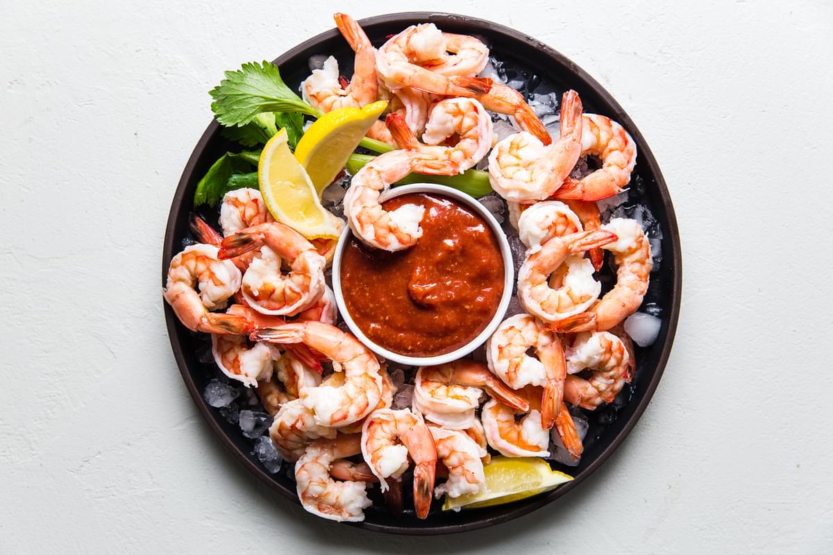 poached shrimp on a serving platter with ice and a bowl of homemade cocktail sauce served with lemon wedges