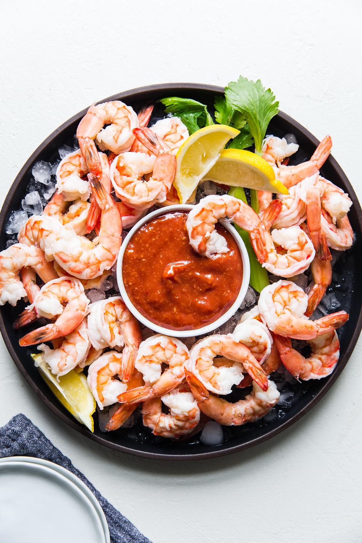 poached shrimp on a serving platter with ice and a bowl of homemade cocktail sauce served with lemon wedges