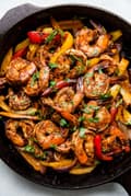 shrimp fajitas in a cast iron skillet with cilantro and bell peppers