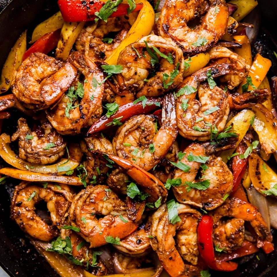 shrimp fajitas in a cast iron skillet with cilantro and bell peppers