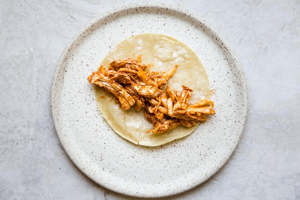 corn tortilla on a plate with shredded chicken and mole sauce