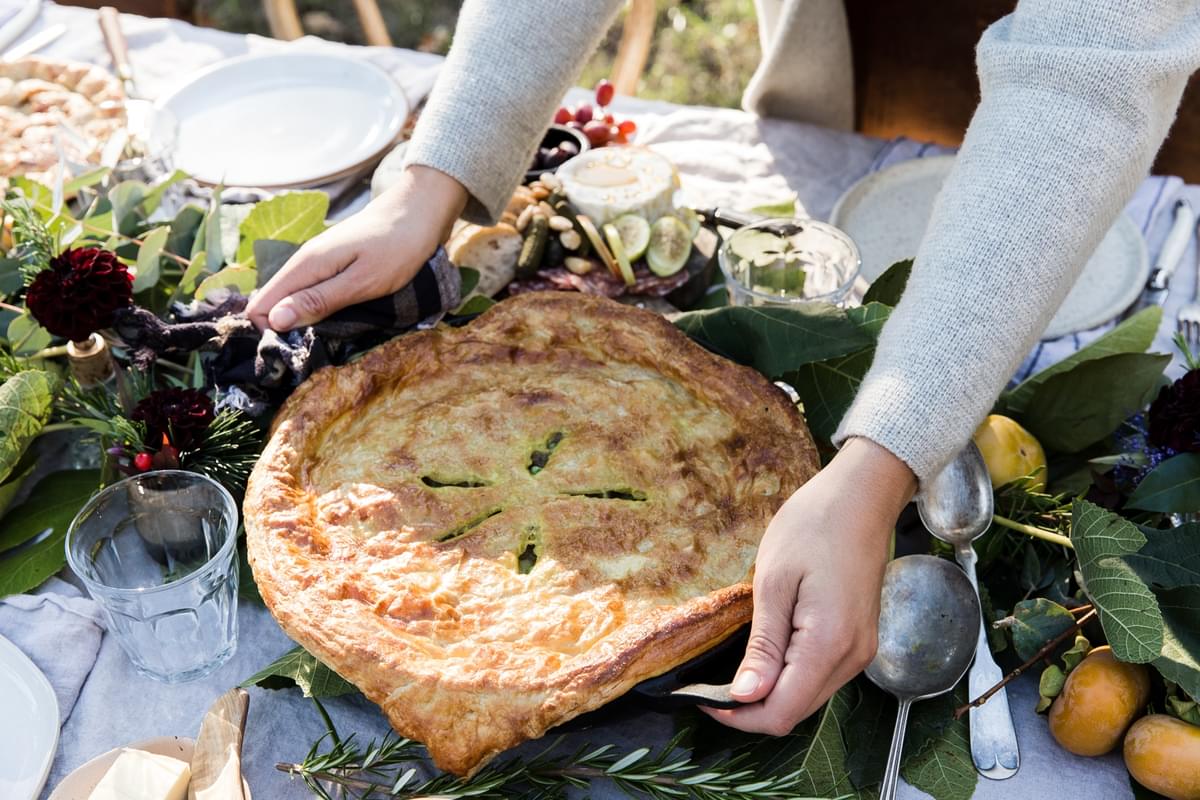 hands setting down a lamb pot pie on an outdoor table