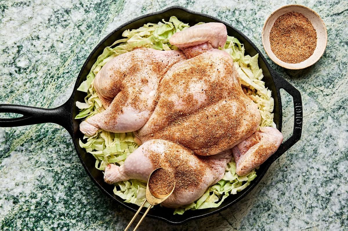 taco seasoning being robbed on a a spatchcocked chicken on top of shredded cabbage seasoned with  salt in a cast iron skillet