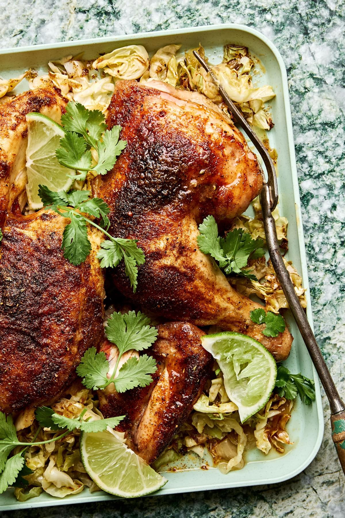 a platter of roasted chicken cut in quarters served on top of cabbage with lime wedges