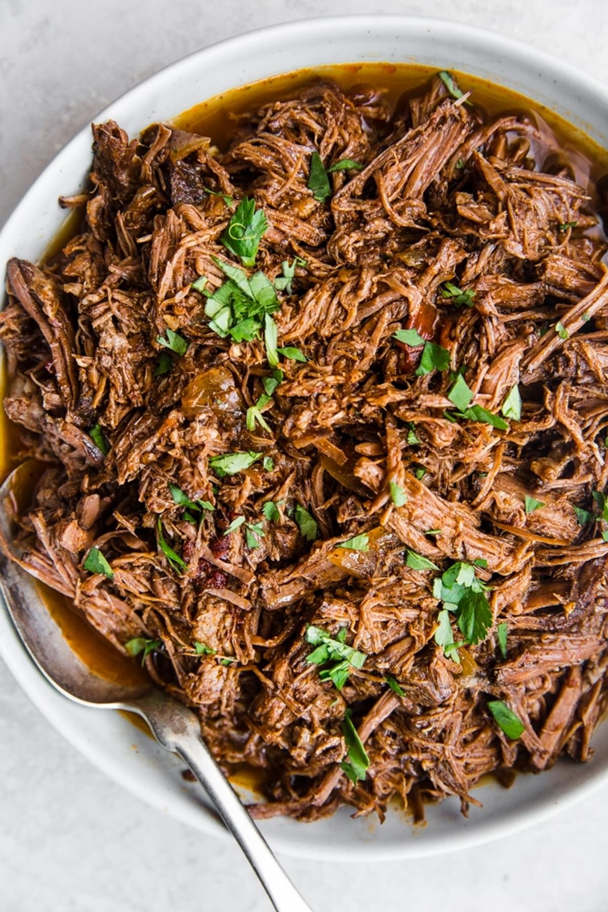 shredded barbacoa meat in a bowl with a serving spoon