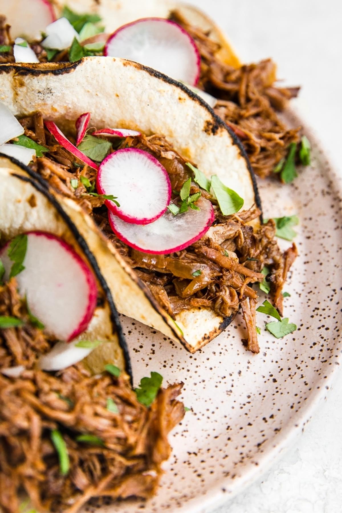 Slow Cooker Barbacoa Beef tacos on a plate with cilantro, onions and radishes