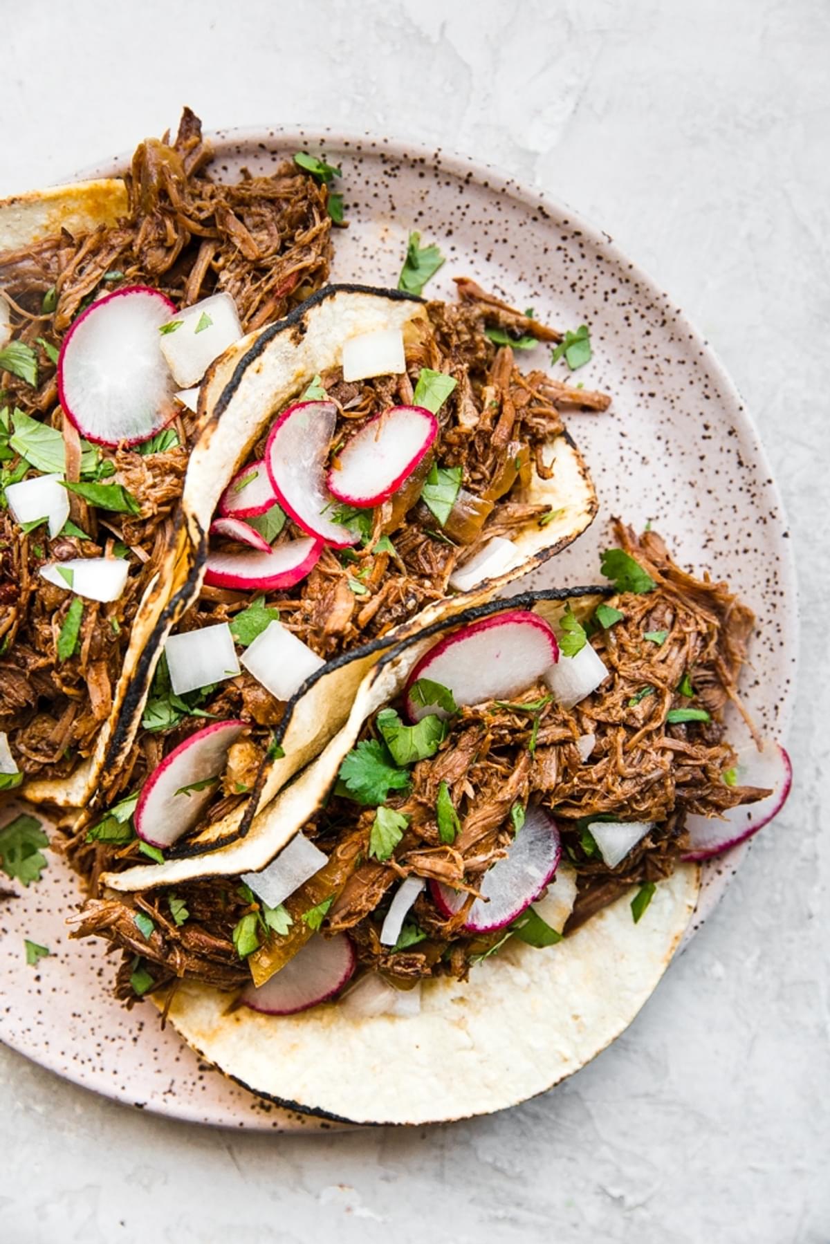 Slow Cooker Barbacoa Beef tacos on a plate with cilantro, onions and radishes