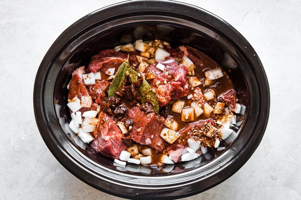 steak, onions, bay leaves and spices in a crock pot for Slow Cooker Barbacoa Beef