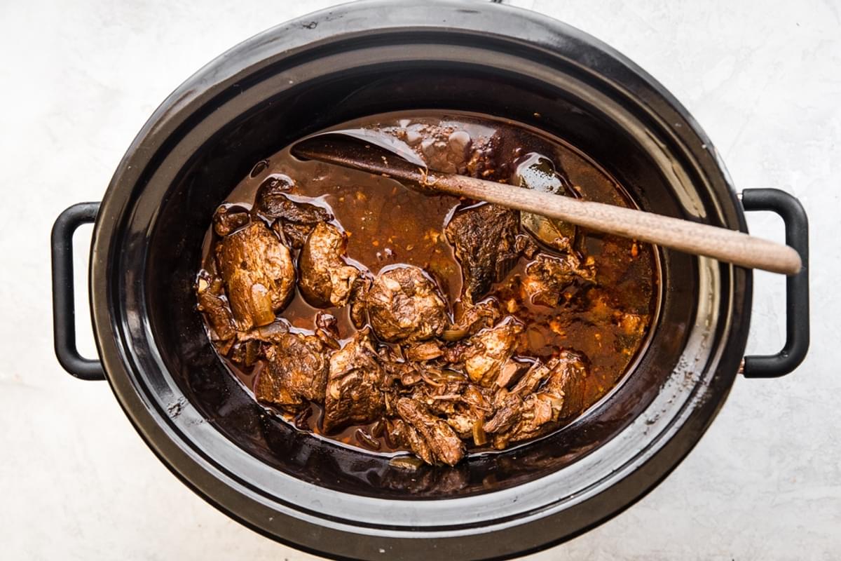 Barbacoa Beef in a crock pot with a wooden spoon