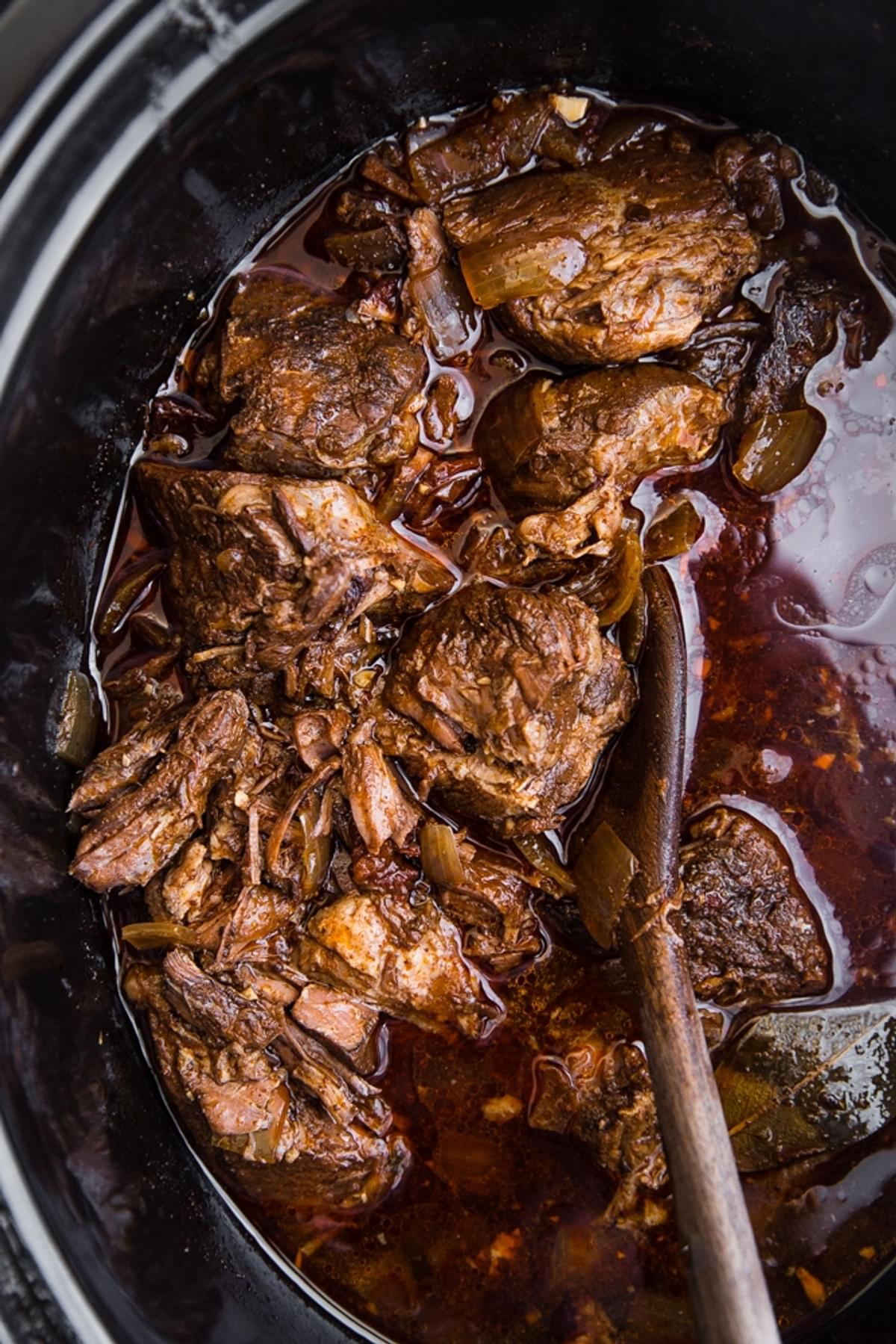 Barbacoa Beef in a crock pot with a wooden spoon