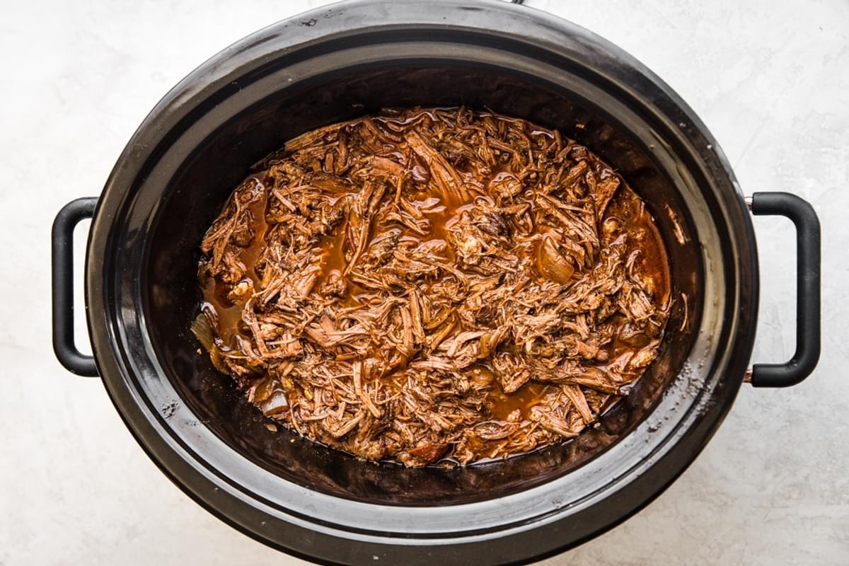 shredded Barbacoa Beef in a crock pot with a wooden spoon