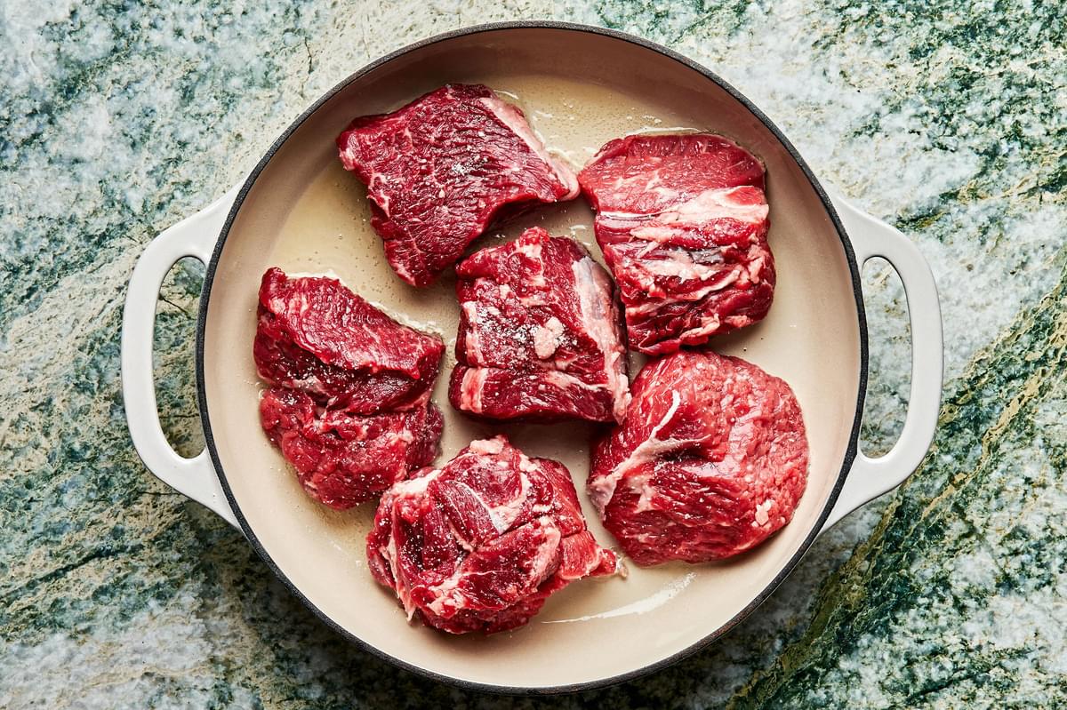 chuck roast cut into 3 in pieces, seasoned with salt, being browned in vegetable oil in a skillet