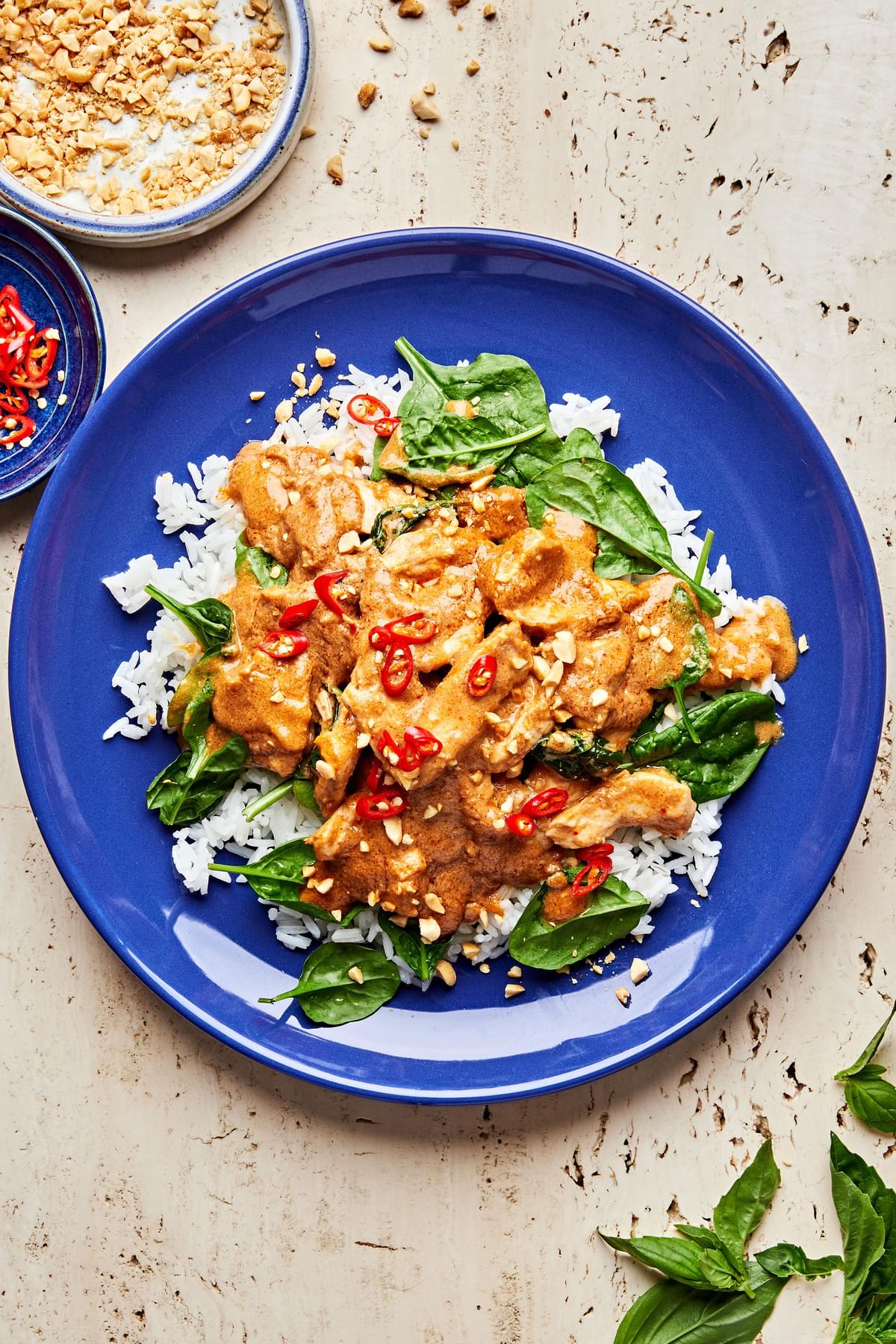 slow cooker swimming rama served on top of white rice topped with crushed peanuts, basil and red chili flakes