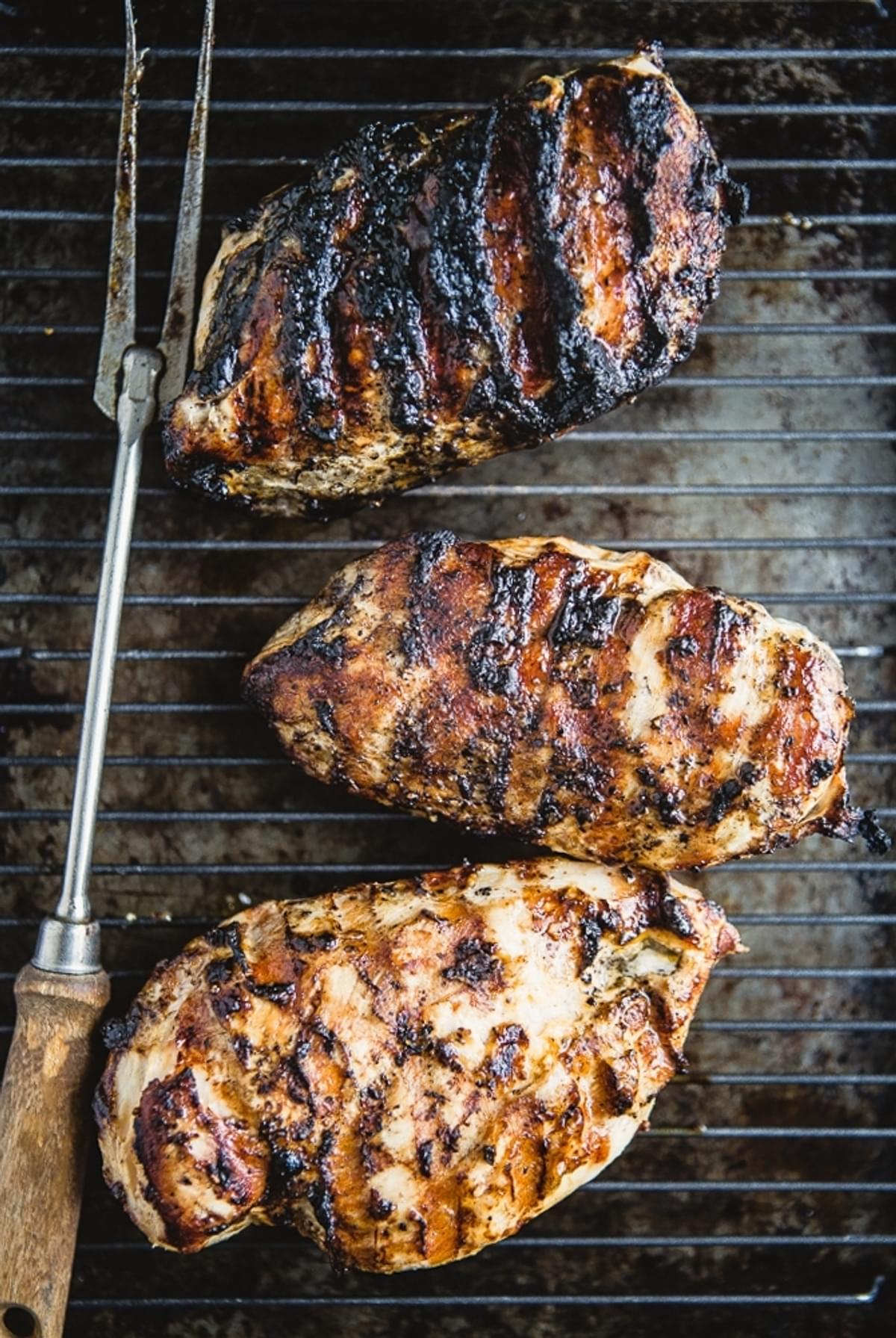 grilled chicken breasts on a cooling rack with a serving fork