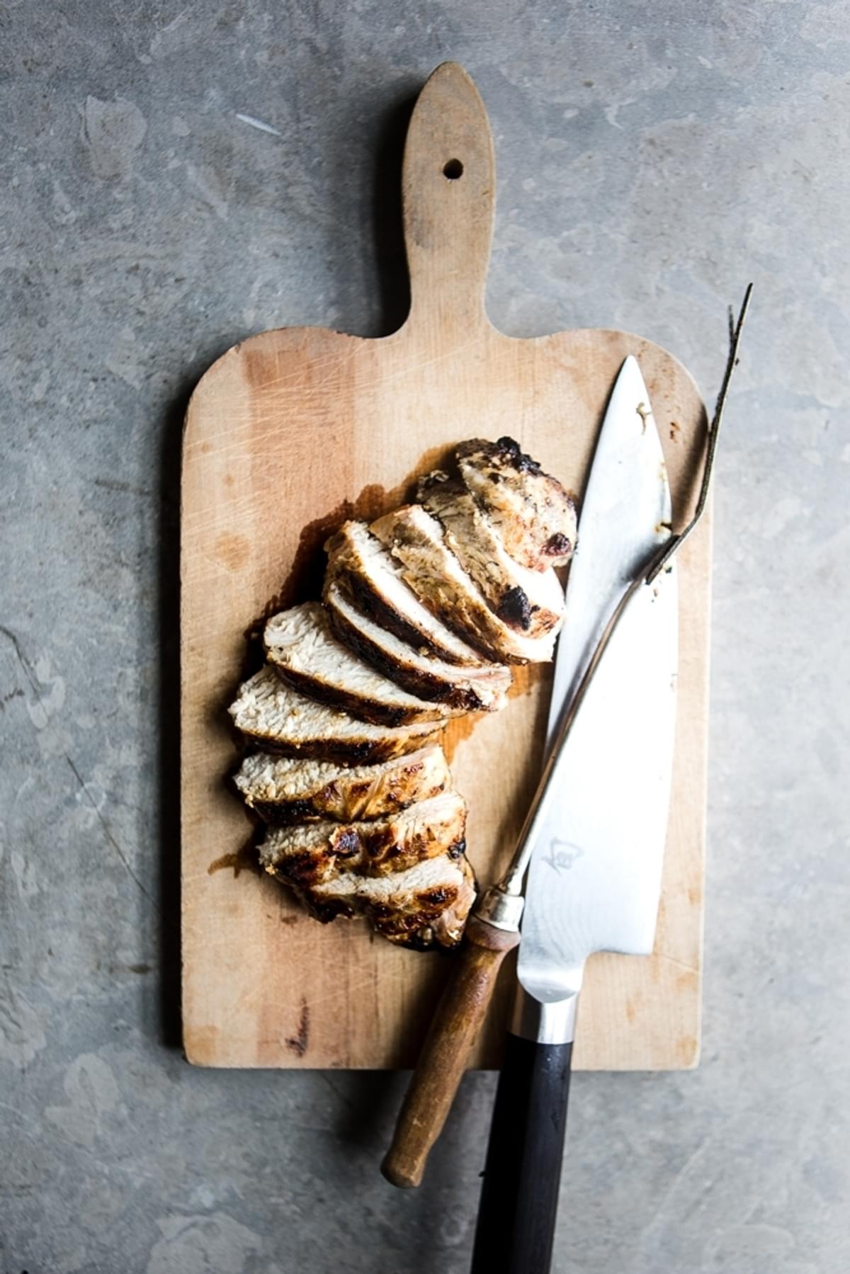 grilled chicken breast sliced on a cutting board with a knife and serving fork