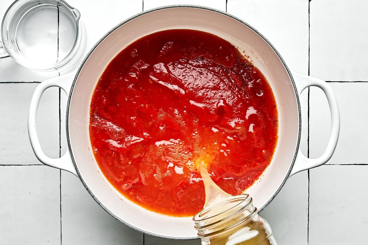 chicken broth being added to a pot with tomato paste, butter, spices and tomato sauce,