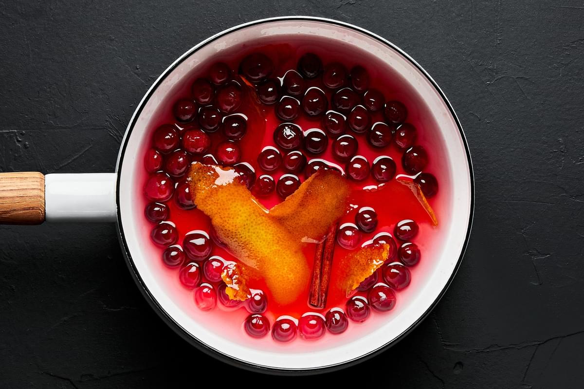 orange peel, cranberries, cinnamon stick, sugar and water simmering in a pot for cranberry-orange simple syrup