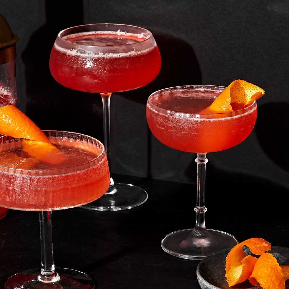 3 spiced bourbon cocktails in coupe glasses made with cranberry-orange simple syrup and garnished with an orange peel  twist