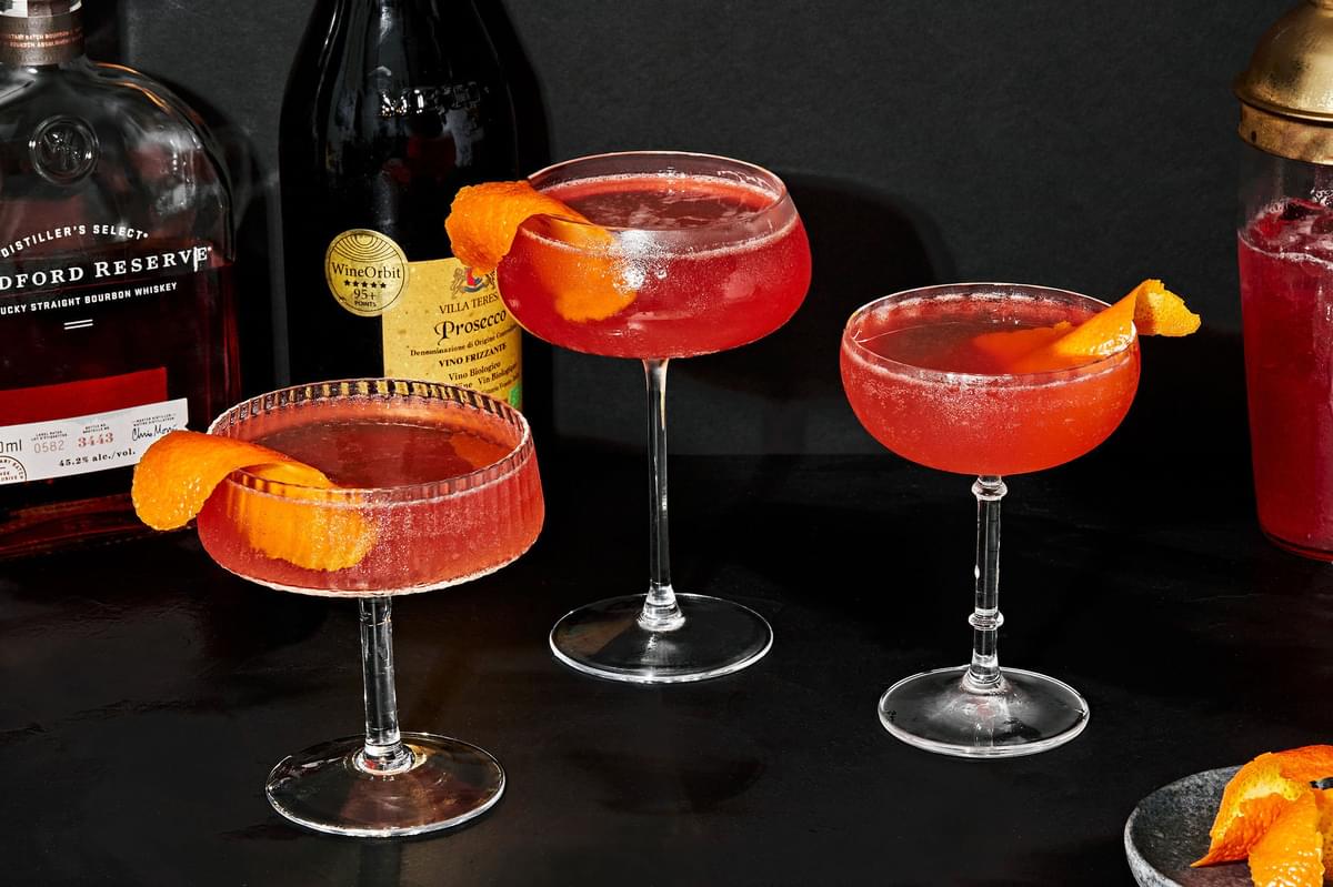 3 spiced bourbon cocktails in coupe glasses made with cranberry-orange simple syrup and garnished with an orange twist