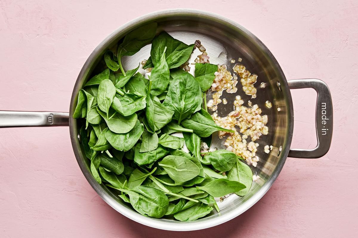 olive oil, shallots and spinach being cooked together in a skillet