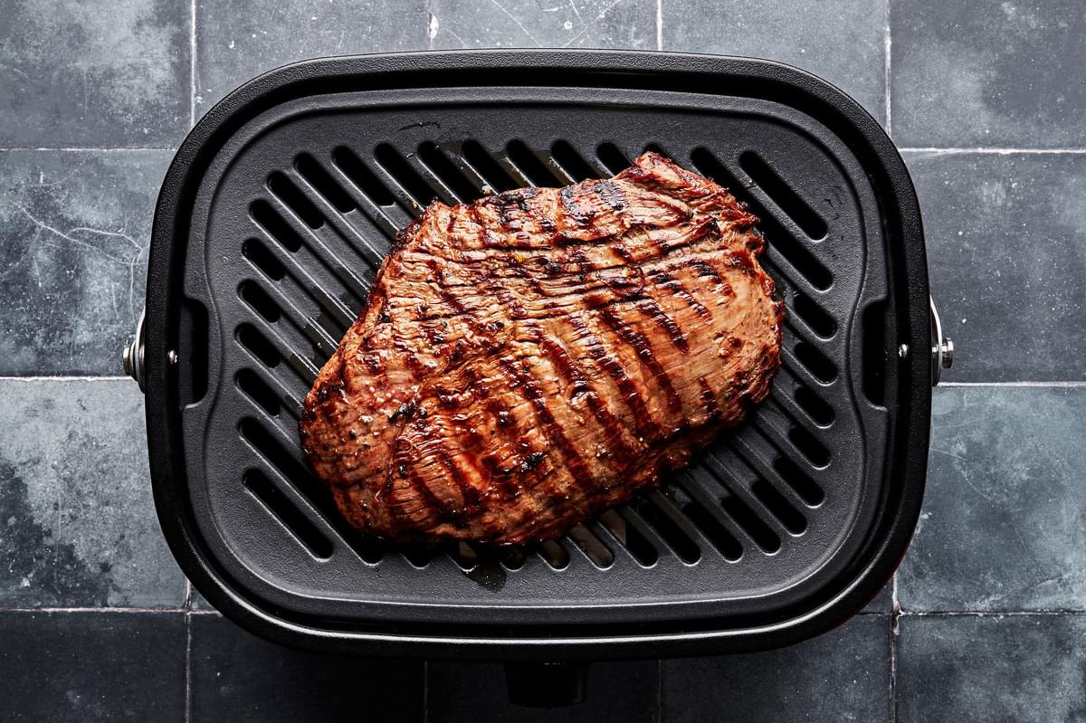 marinated flank steak being cooked on a grill