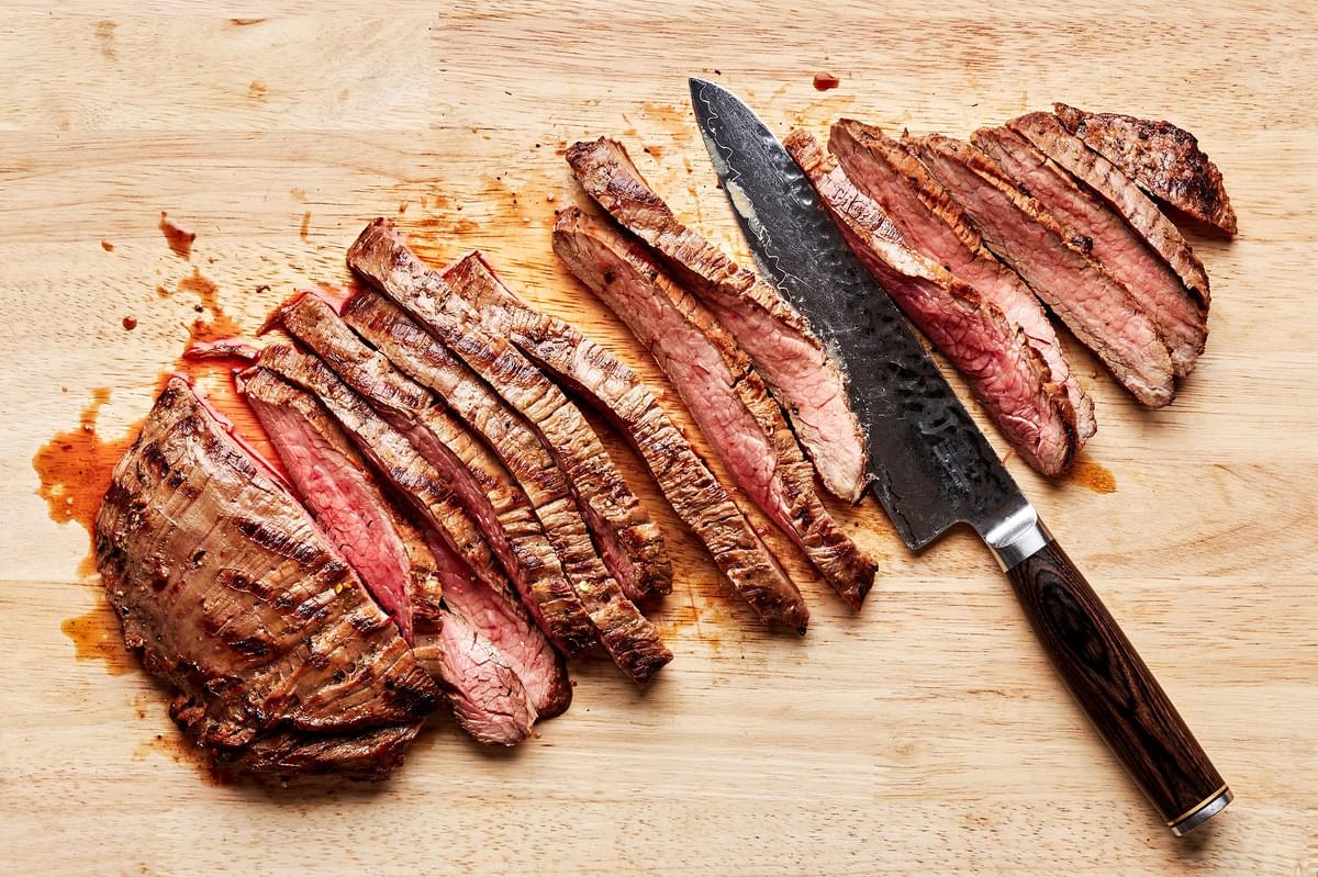 grilled flank steak being sliced on a cutting board
