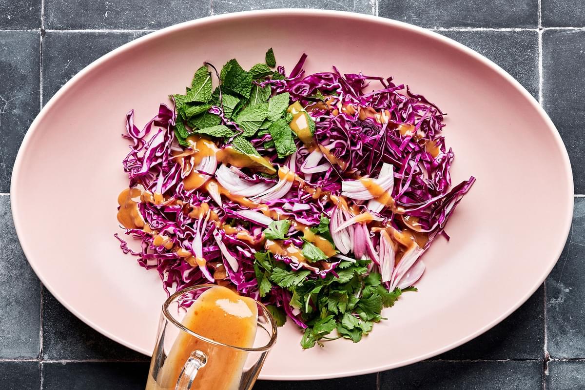 cabbage, mint, cilantro and shallots in a bowl being drizzled with thai salad dressing
