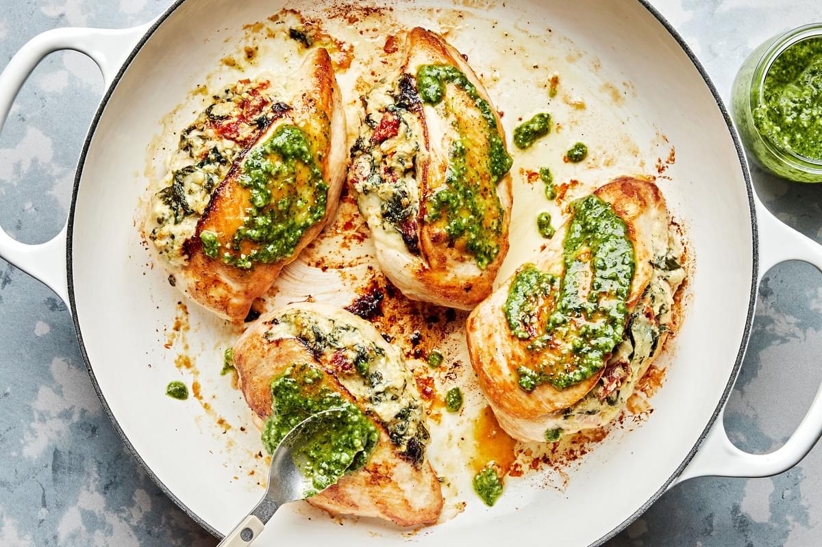 chicken breast stuffed with spinach, garlic, cream cheese, mozzarella, sun-dried tomatoes and pesto being cooked in a skillet