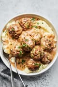 a bowl of homemade swedish meatballs served on top of mashed potatoes sprinkled with parsley