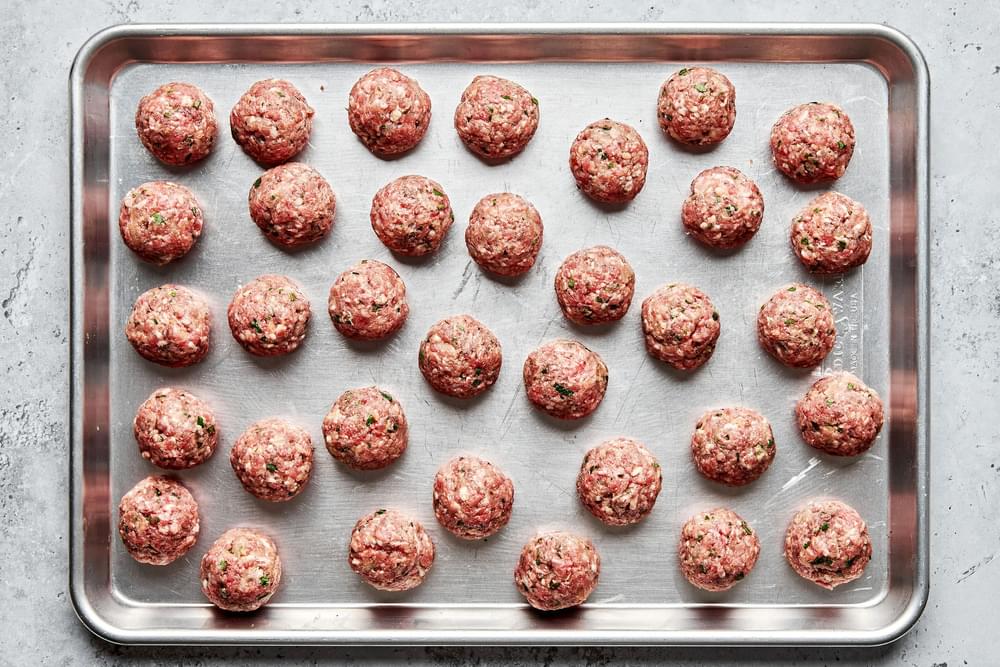 raw meatballs on a baking sheet made with beef, pork, parsley, spices, grated onion, panko and eggs