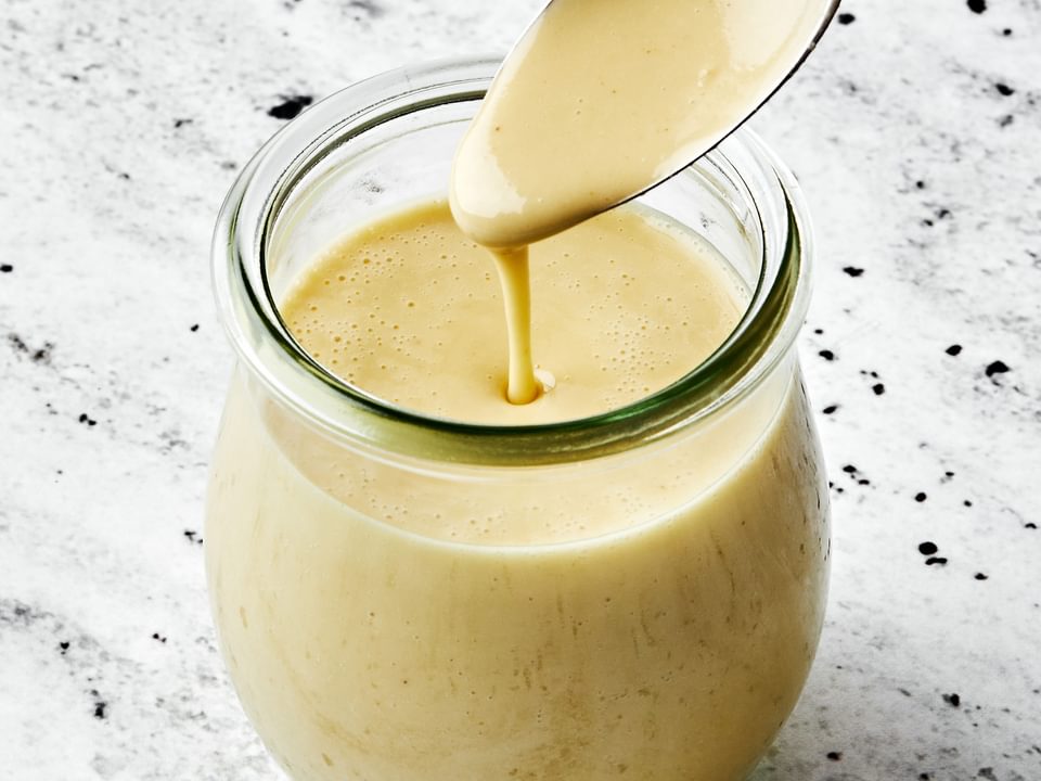 homemade tahini dressing in a jar with a spoon made with  tahini, olive oil, apple cider vinegar,, sesame oil, honey & spices
